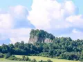 Skalisty szczyt porośnięty drzewami, przypominający wilczą górę, góruje nad zielonymi polami i lasami.