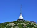 Wieża telewizyjna Ještěd w Liberec, Czechy, góruje nad zielonym wzgórzem pod błękitnym niebem.