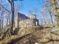 Kamienne ruiny zamku Bolczów w otoczeniu nagich drzew, z drewnianym mostkiem prowadzącym do wejścia.