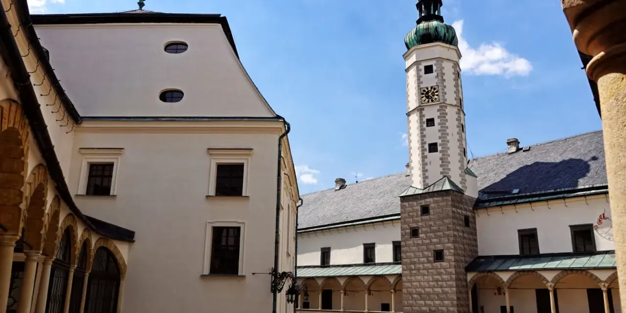 Dziedziniec zamku w Bruntalu, Czechy. Białe mury, arkadowe krużganki i wysoka wieża zegarowa pod błękitnym niebem.