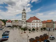 Rynek w Paczkowie, polskie Carcassonne, z ratuszem i wieżą. Brukowany plac, samochody, ławki i małe drewniane budki.