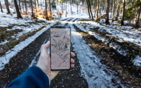 Telefon z mapą pokazuje szlak w lesie. Widać ślady śniegu na drodze, a na ekranie zaznaczony jest skopiec szlak.