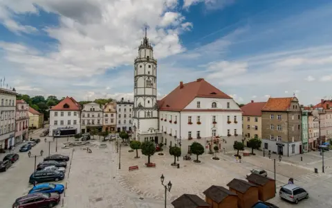 Rynek w Paczkowie, polskie Carcassonne, z ratuszem i wieżą. Brukowany plac, samochody, ławki i małe drewniane budki.