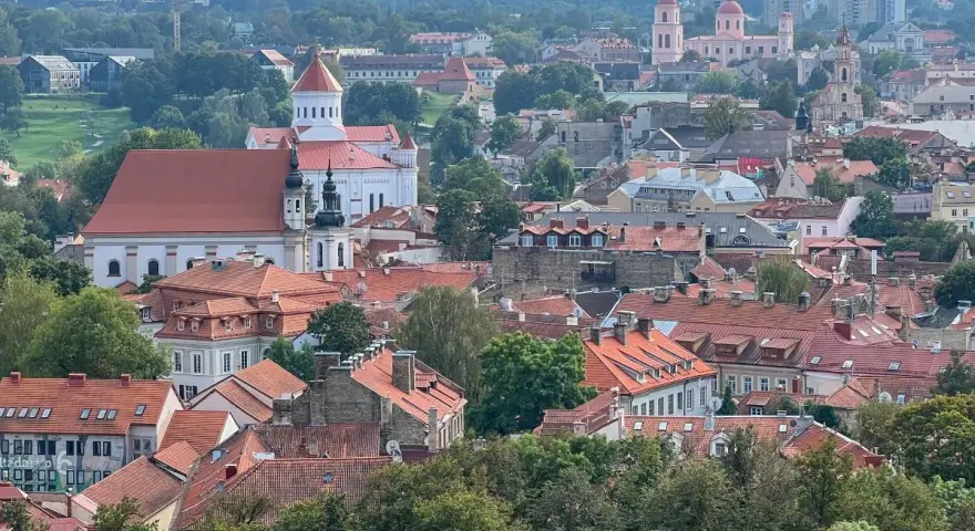 Widok na Wilno z wzgórza Giedymina. Czerwone dachy, białe kościoły i zielone drzewa tworzą malowniczy krajobraz.
