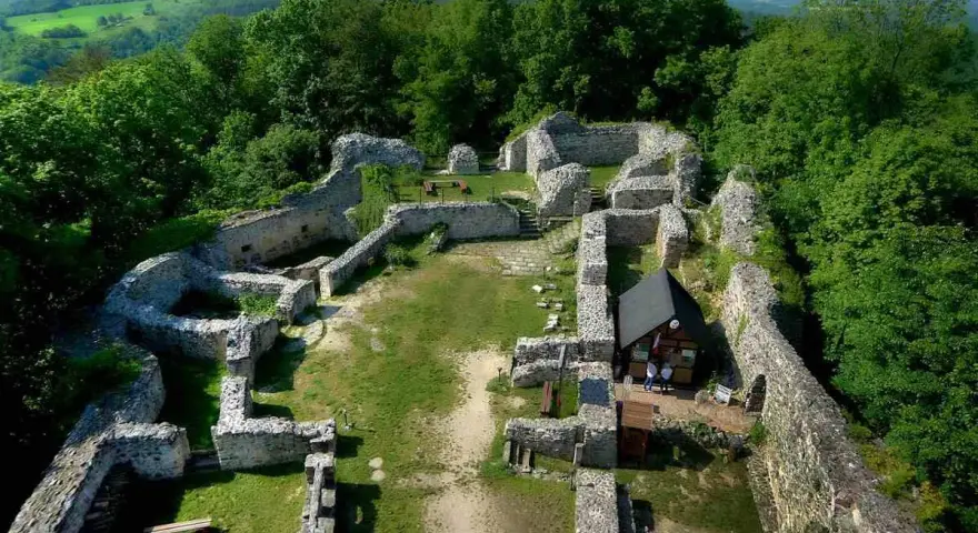 Ruiny zamku lenno otoczone zielenią, z widokiem na pagórkowaty krajobraz.