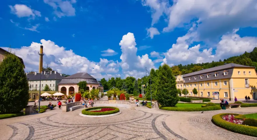 Słoneczny dzień w Kudowie Zdrój. Spacerowicze odpoczywają w pięknym parku zdrojowym, otoczonym zabytkową architekturą.