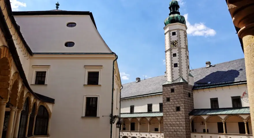 Dziedziniec zamku w Bruntalu, Czechy. Białe mury, arkadowe krużganki i wysoka wieża zegarowa pod błękitnym niebem.