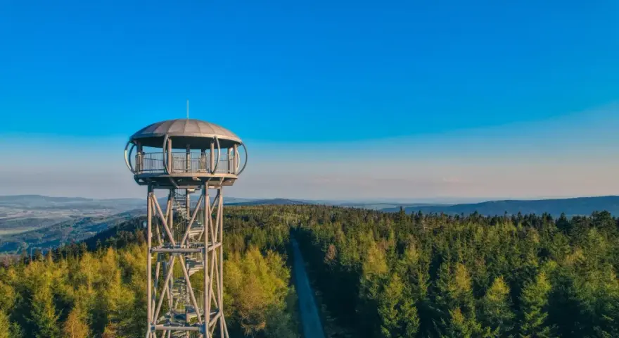 Metalowa jagodna wieża widokowa wznosi się nad gęstym lasem iglastym, oferując zapierającą dech w piersiach panoramę.