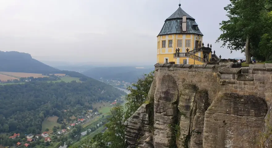 Żółty pałac na skale, część twierdzy Königstein, góruje nad doliną rzeki i lasami.
