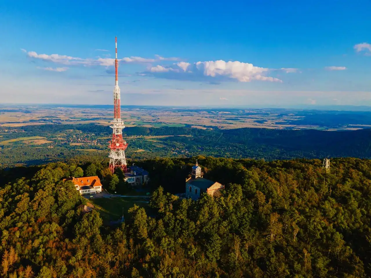 Wieża RTV na szczycie góry, otoczona lasem. Widać budynki i rozległą panoramę. Idealne miejsce na wędrówkę po ślęża szlaki.