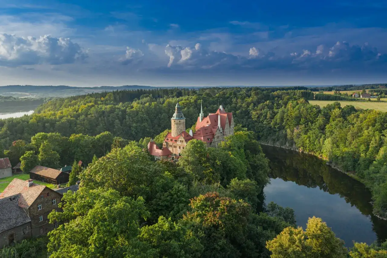 Malowniczy zamek na wzg&oacute;rzu otoczony lasem, jeden z wielu pięknych zamk&oacute;w Dolnego Śląska, nad spokojną rzeką.