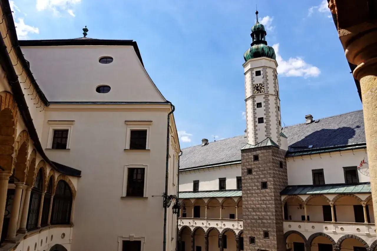 Dziedziniec zamku w Bruntalu, Czechy. Białe mury, arkadowe krużganki i wieża zegarowa pod błękitnym niebem.