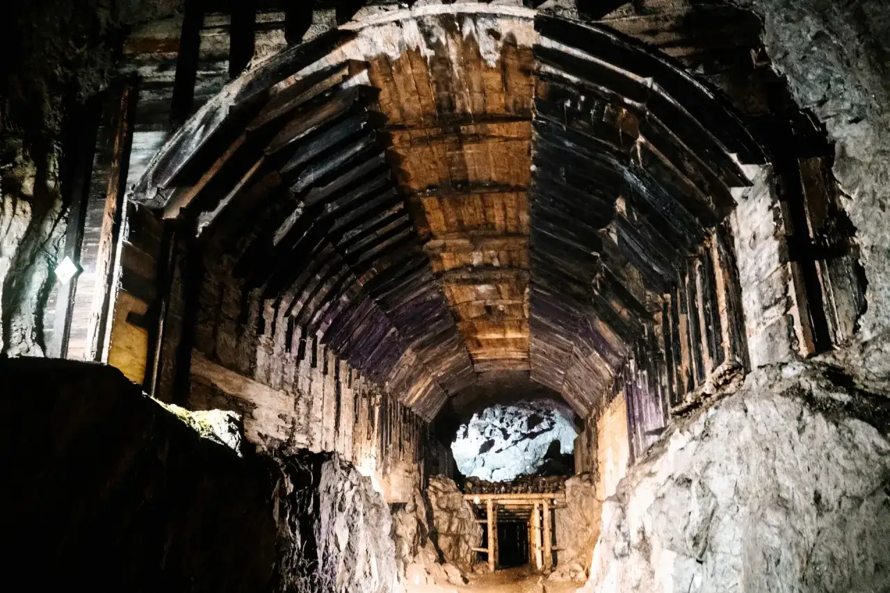 Wnętrze tunelu w podziemnym mieście Osówka, z drewnianymi stropami i kamiennymi ścianami, prowadzi w głąb mroku.